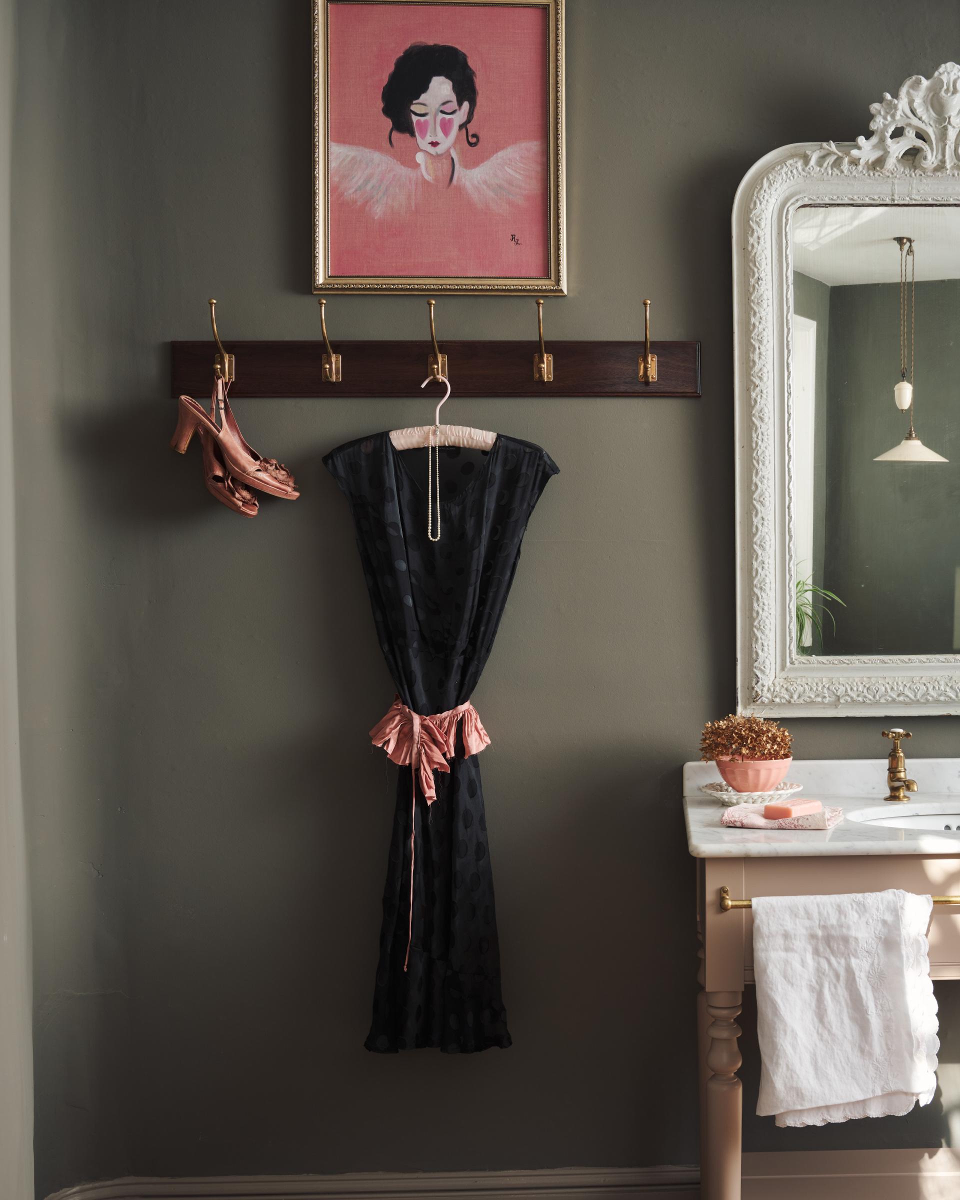 A Mahogany Finish Hook Rack with 5 Edwardian brass hooks, fitted to a moody grey wall with a black dress and dusky pink shoes hanging. A pink portrait painting and tall mirror decorate the space around the hook rack.