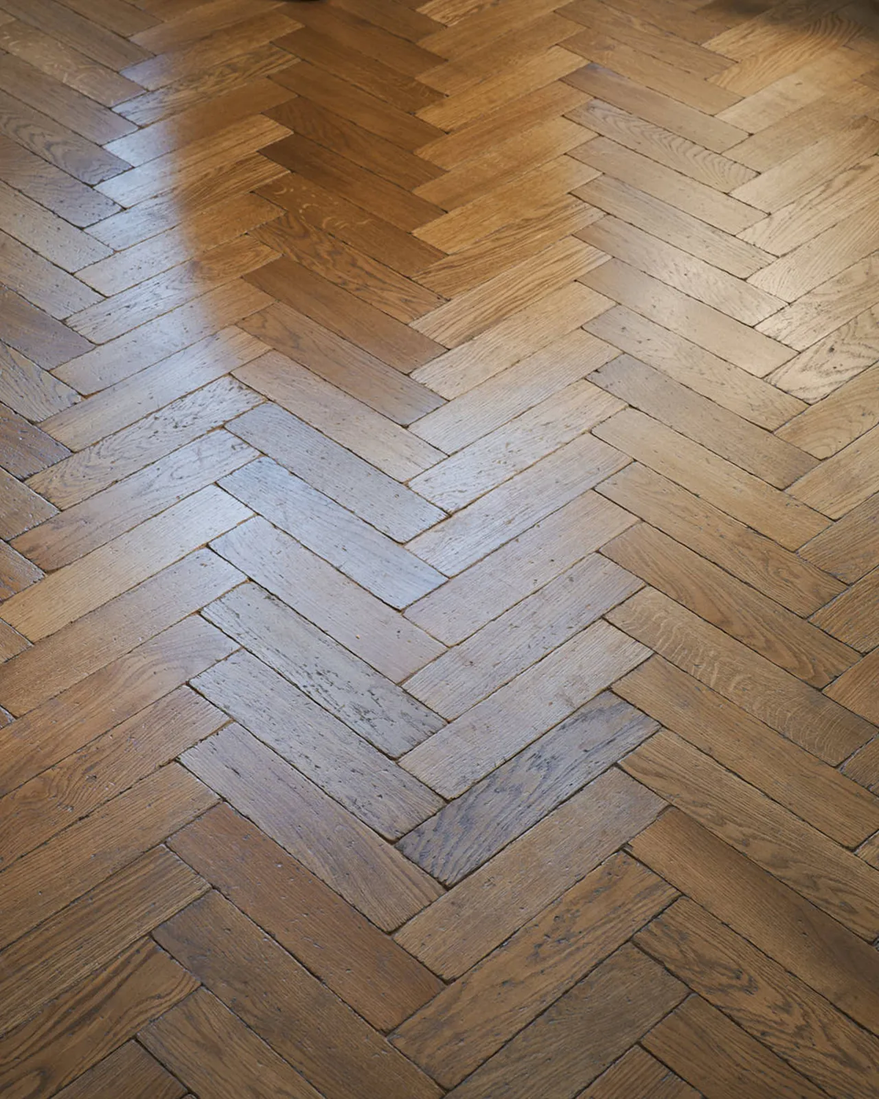 A close-up, angled view of an oak parquet flooring with a warm aged finish.