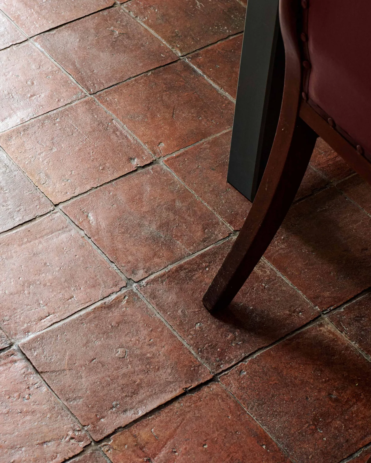 An oblique view of square terracotta flooring with an authentic aged finish and an antique chair on top.