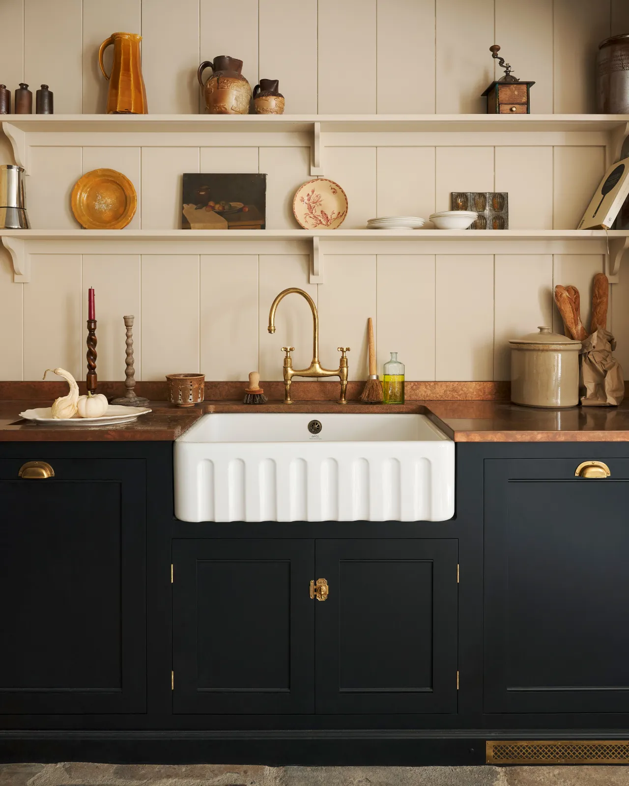 A straight-on view of a Victorian-inspired rack and pinion cupboard catch in a warm burnished brass finish, fitted to a black painted Georgian-style kitchen sink cabinet with a fluted Belfast sink and aged copper worktop.