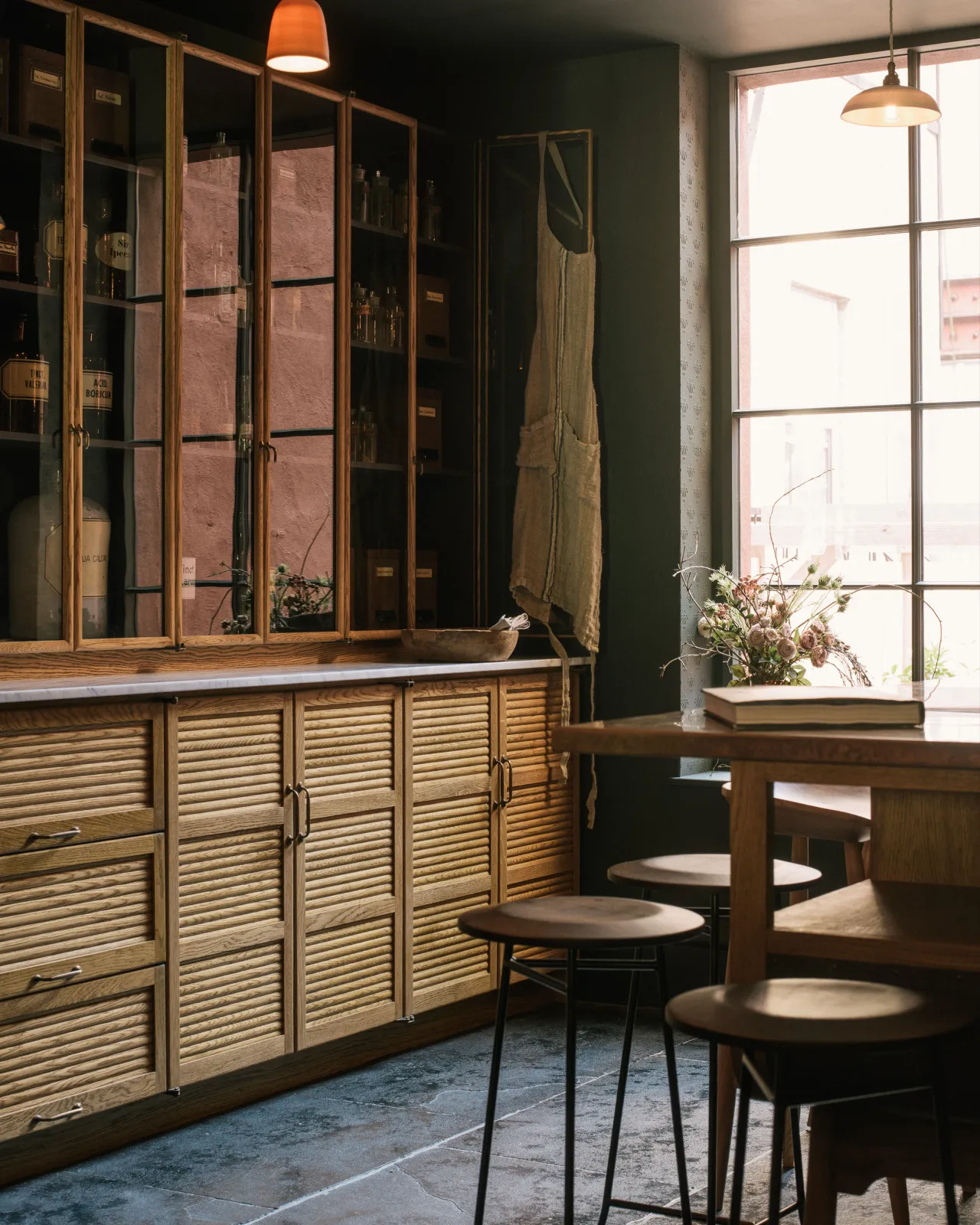 An oblique view of the Haberdasher's display in deVOL's New York showroom, with a combination of tambour-fronted and glazed cupboards and beautifully aged, Brushed Charcoal Limestone flooring.