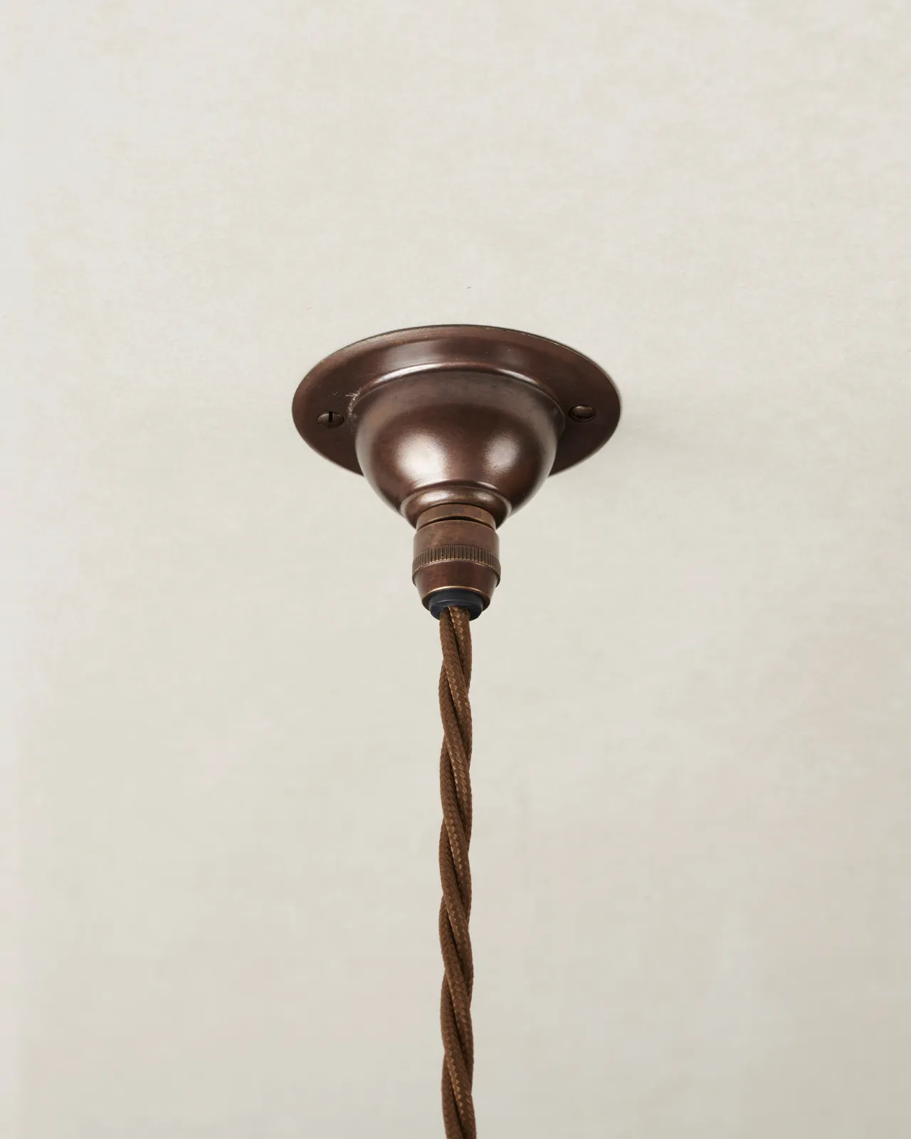 A small aged brass ceiling rose with a brown twisted fabric flex cord.