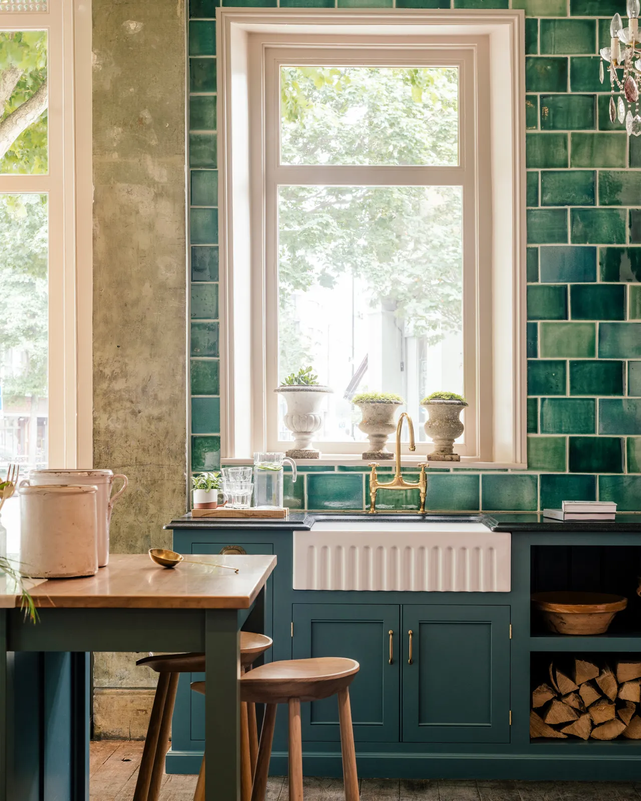 Emerald green wall tiles surround a beautiful original window in a Victorian townhouse, a traditional English kitchen with a fluted Belfast sink and brass mixer tap are below.