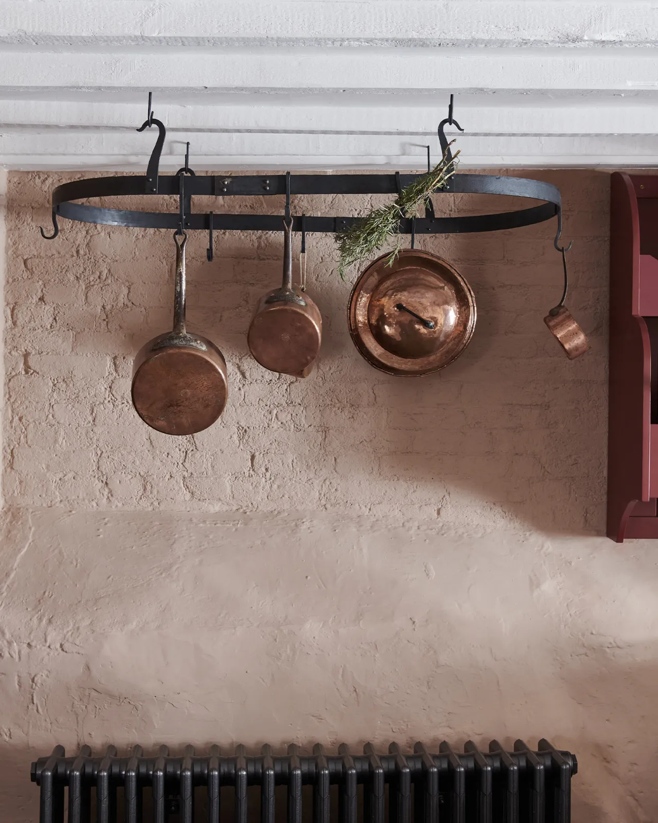 A straight-on view of a large oval-shaped wrought iron pot hanger suspended from a beamed ceiling via iron hooks.