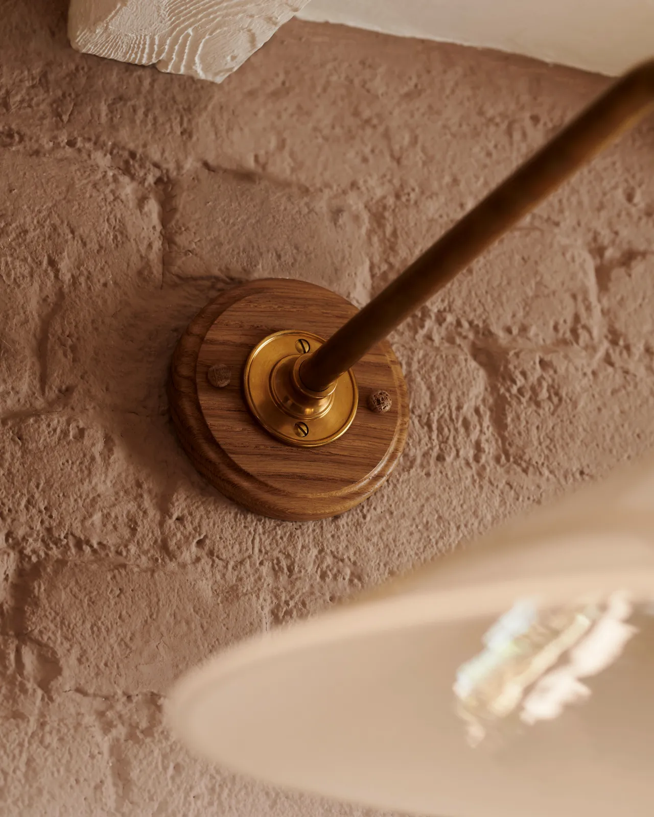 A close-up view of the oak pattress and brass arm of a small Victorian-inspired wall light.
