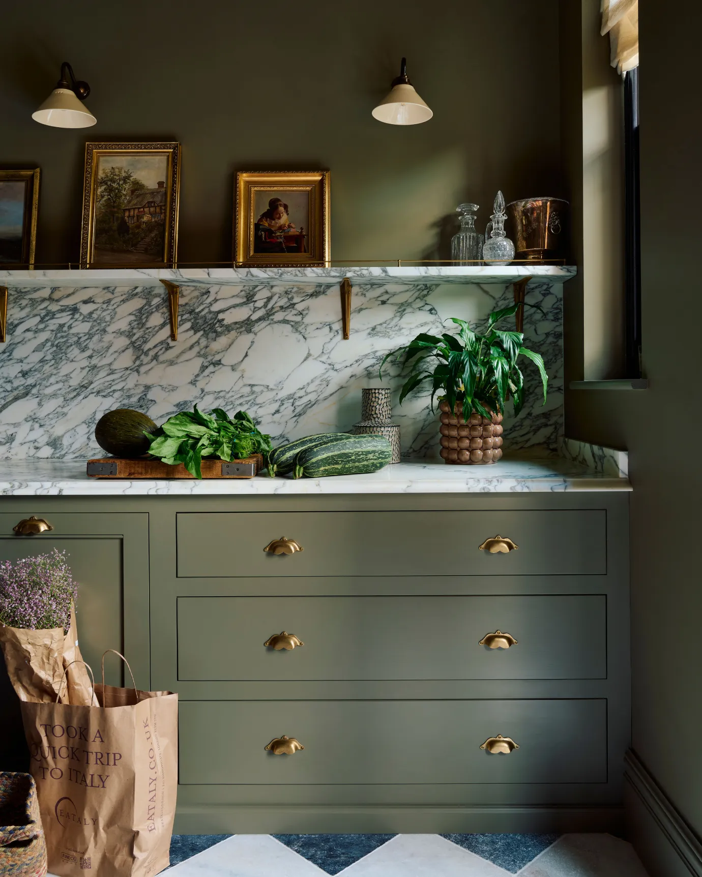 A straight-on view of a moody sage green coloured kitchen with a set of three wide pan drawers, each with two bohemian-style cup handles in an aged brass finish.