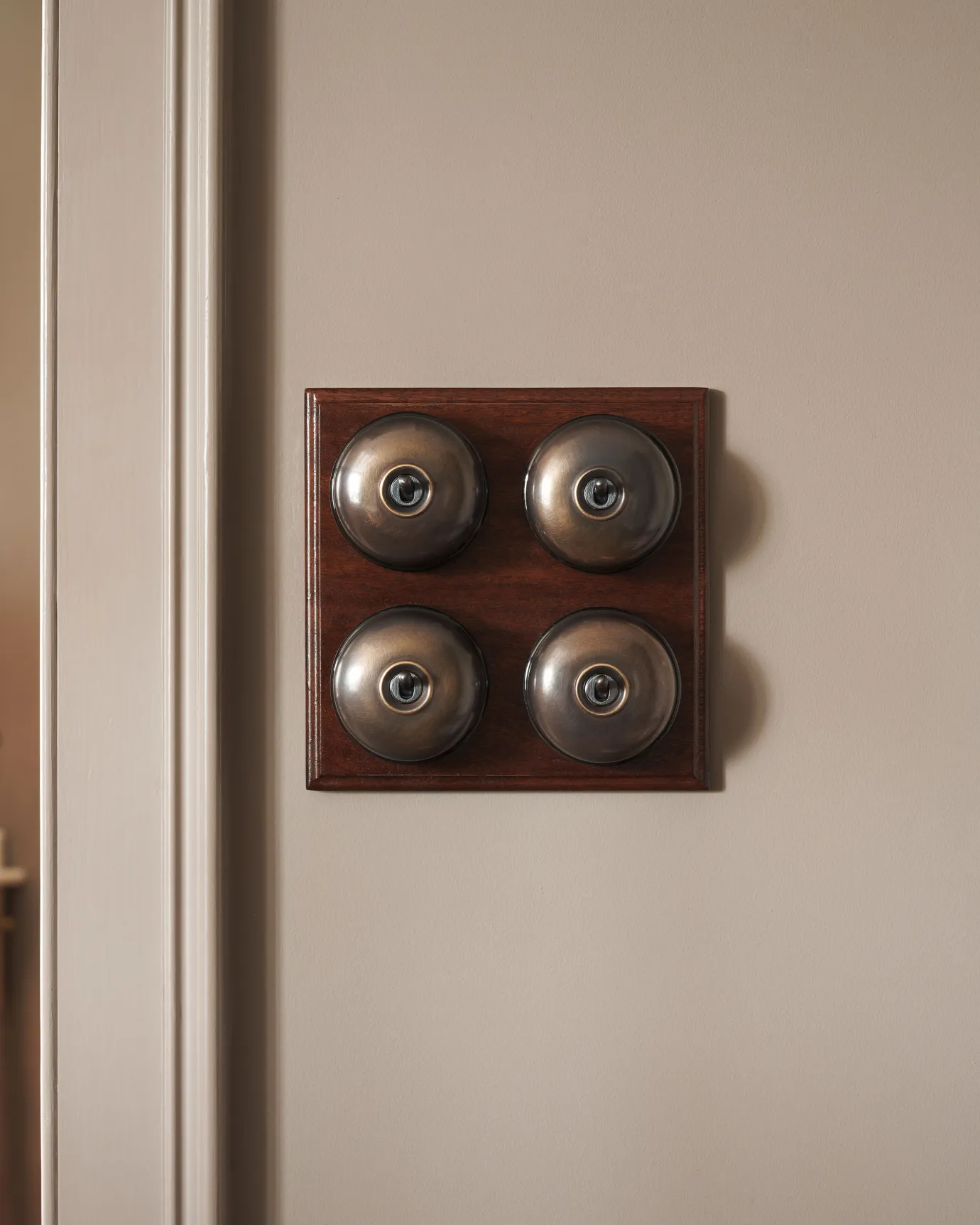 A 4 gang bank of Dolly toggle light switches in an Oxidised Brass finish, with black ceramic bases and a Stained Sapele pattress.