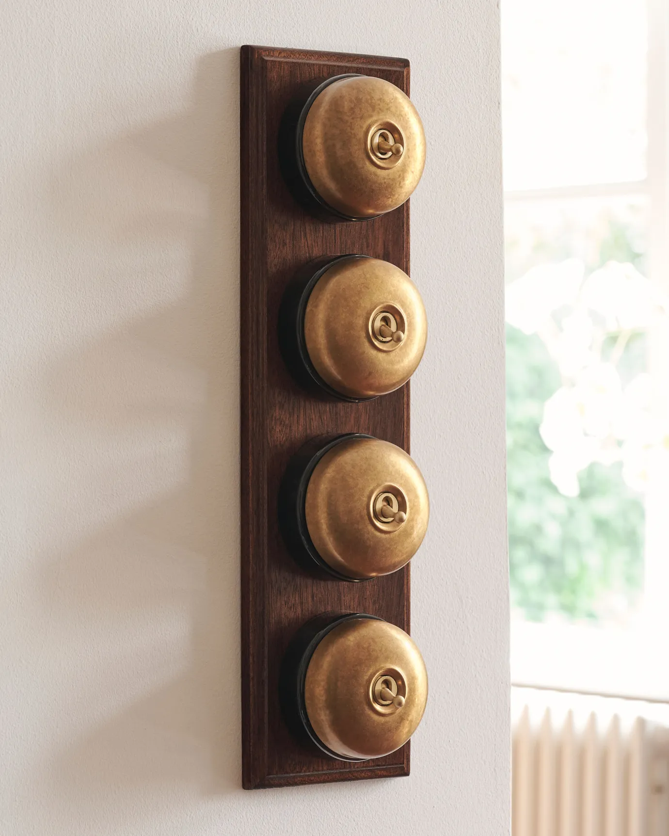 A 4 gang row of Dolly toggle light switches in an Aged Brass finish, with black ceramic bases and a Stained Sapele pattress.