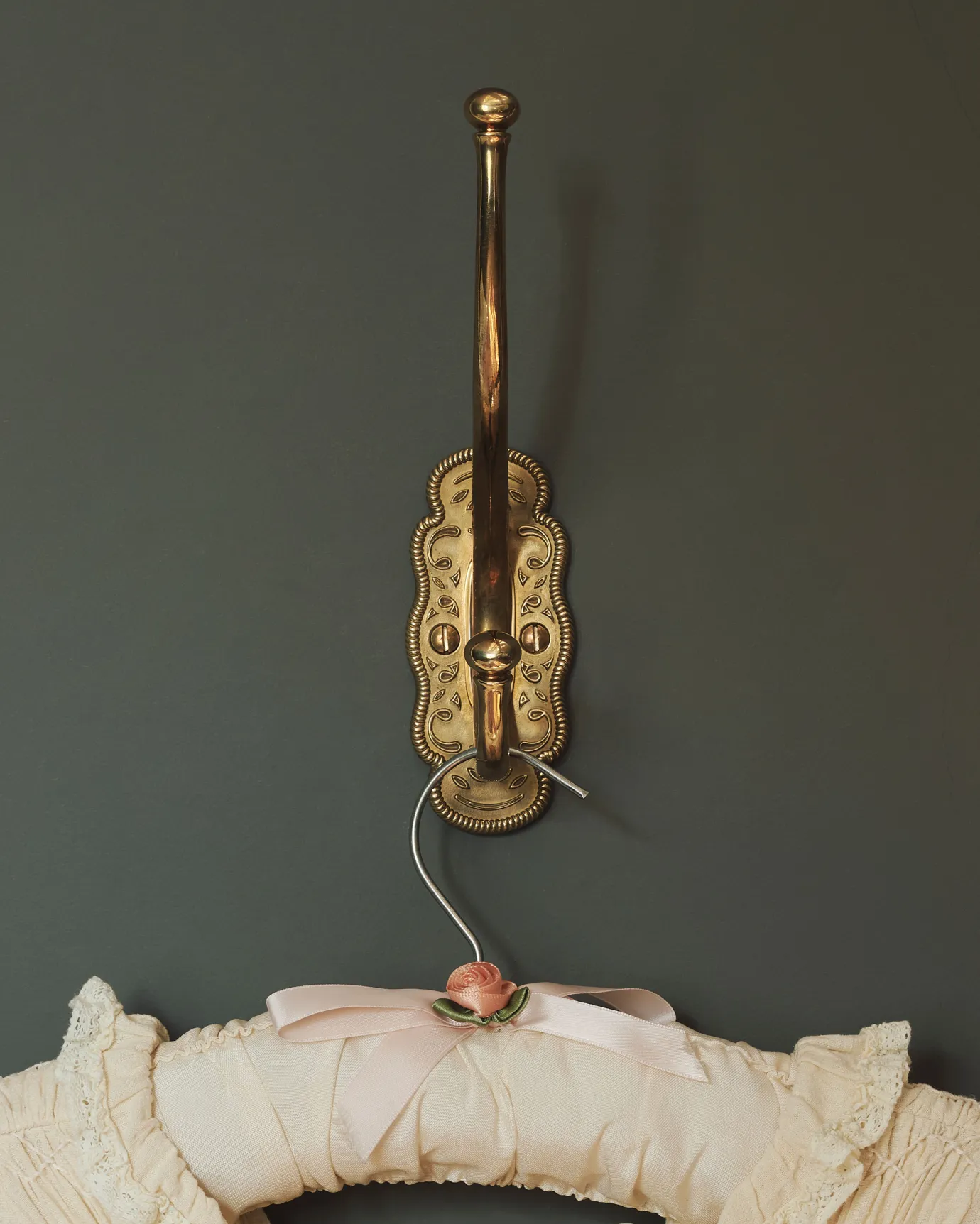 A large Parisian café-style brass hook, fitted to a grey painted wall.