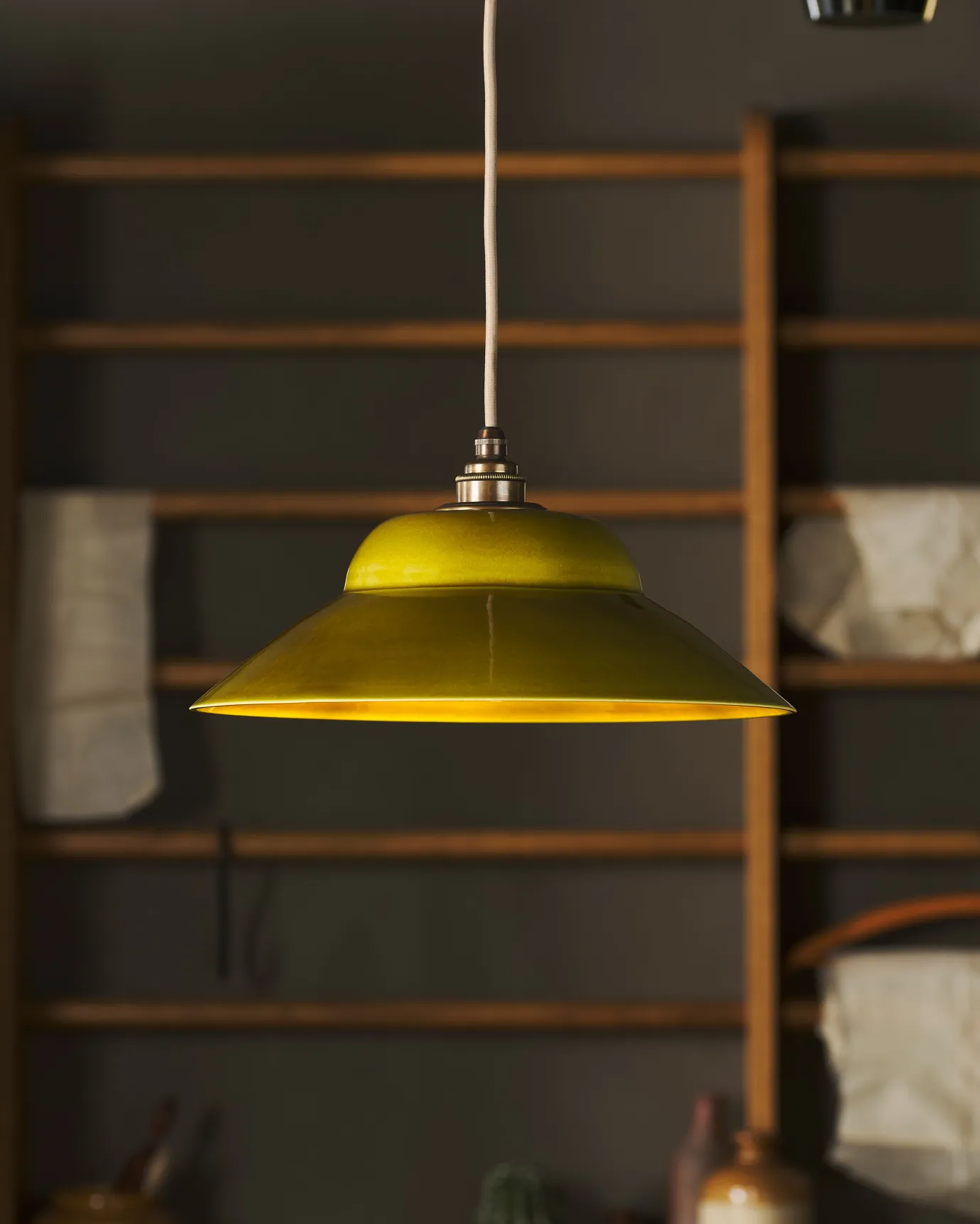 A straight-on view of a mid-century-style chartreuse glazed ceramic pendant light in front of oak racking.