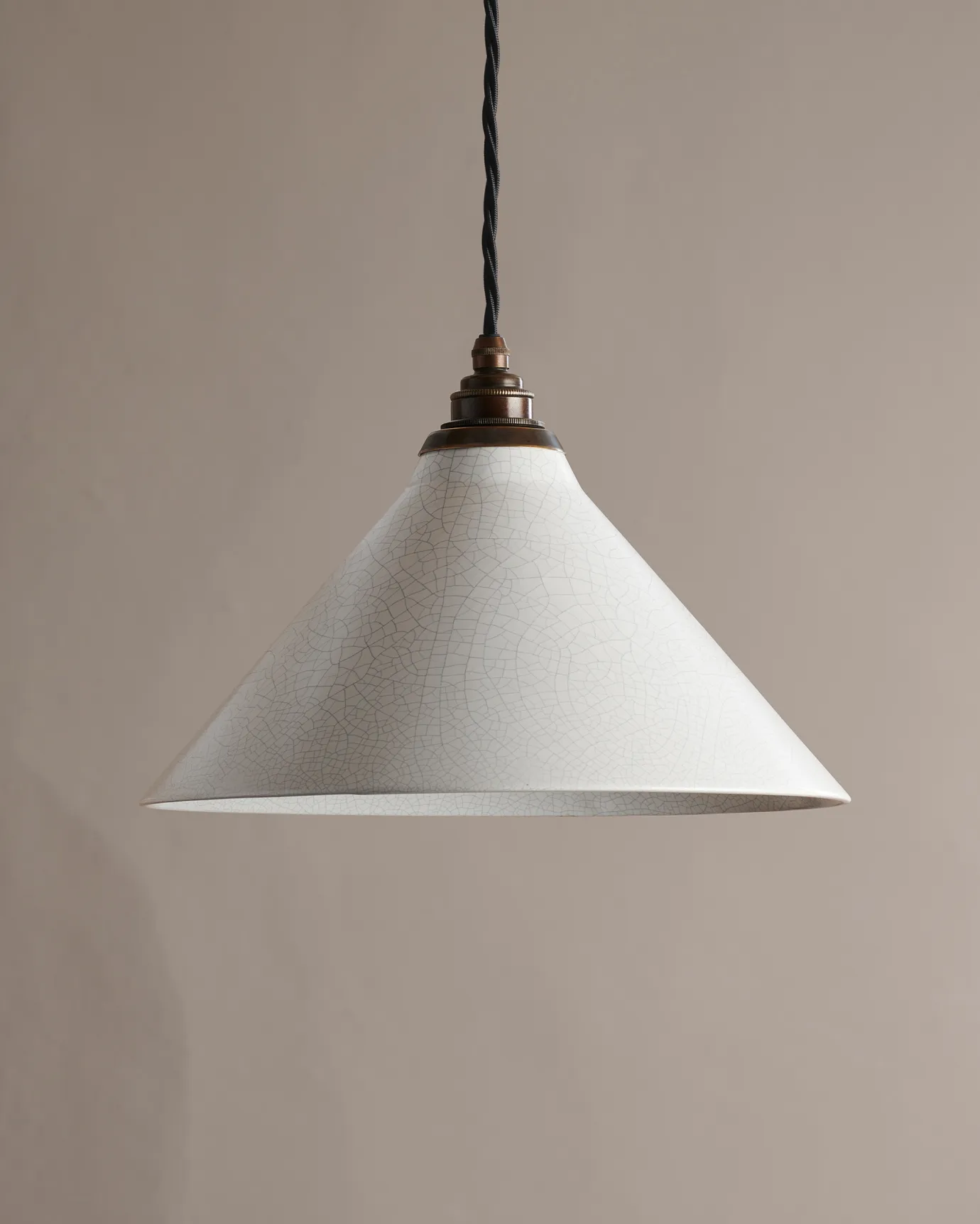 A large white glazed ceramic pendant light with delicate crazing, an antiqued brass E27 lampholder and cuff and black twisted fabric flex cord.