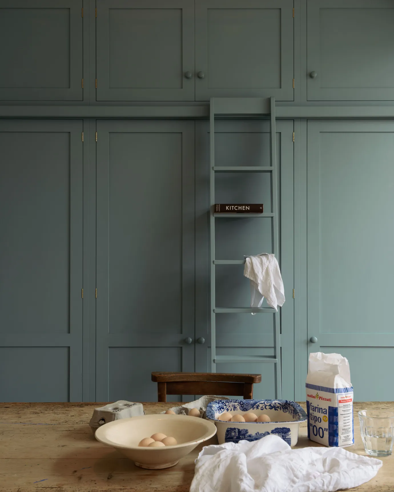 A straight-on view of a tall bank of duck-egg blue painted Shaker-style pantry cupboards with a sliding ladder.