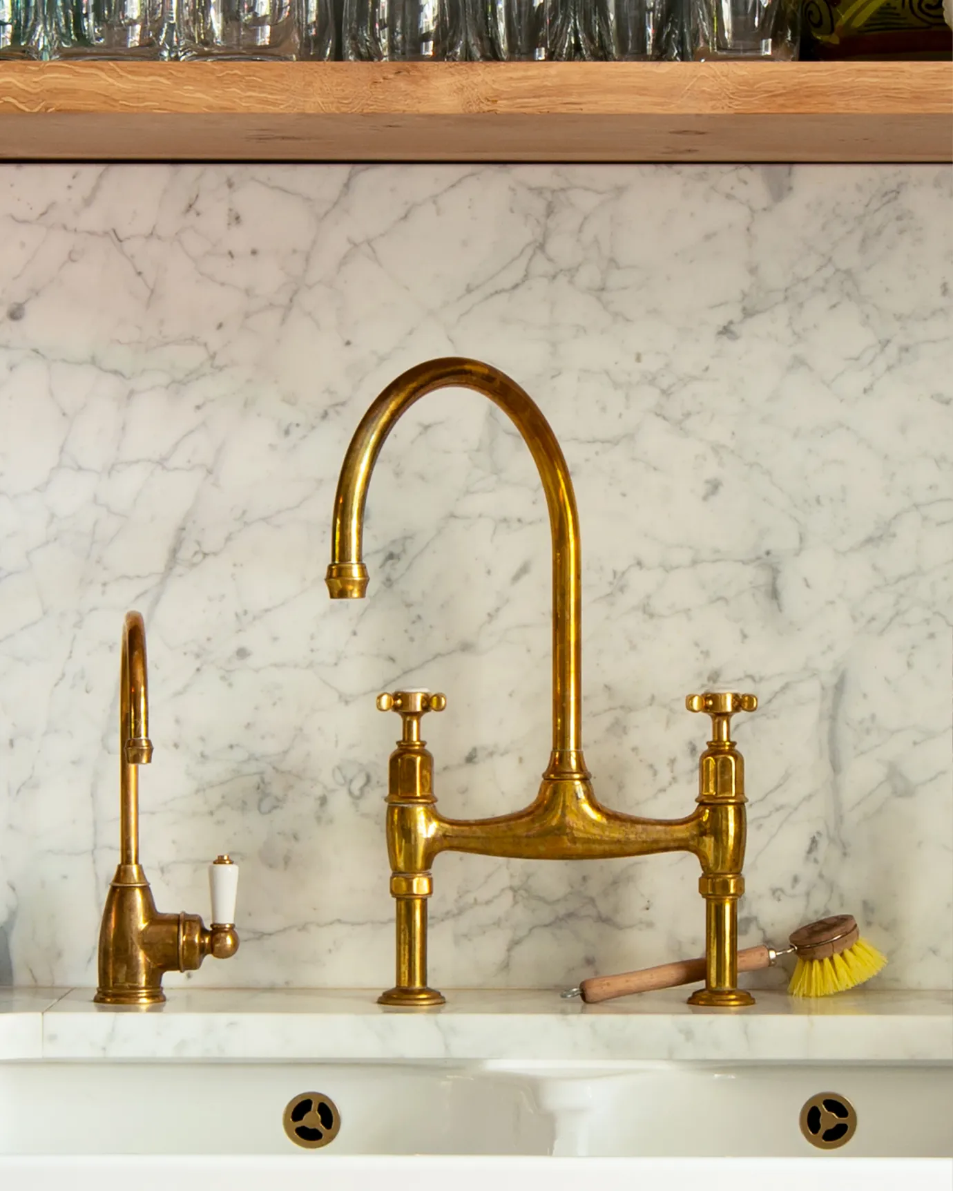A straight-on view of a small traditional-style aged brass tap with a white ceramic lever beside a larger aged brass mixer tap.