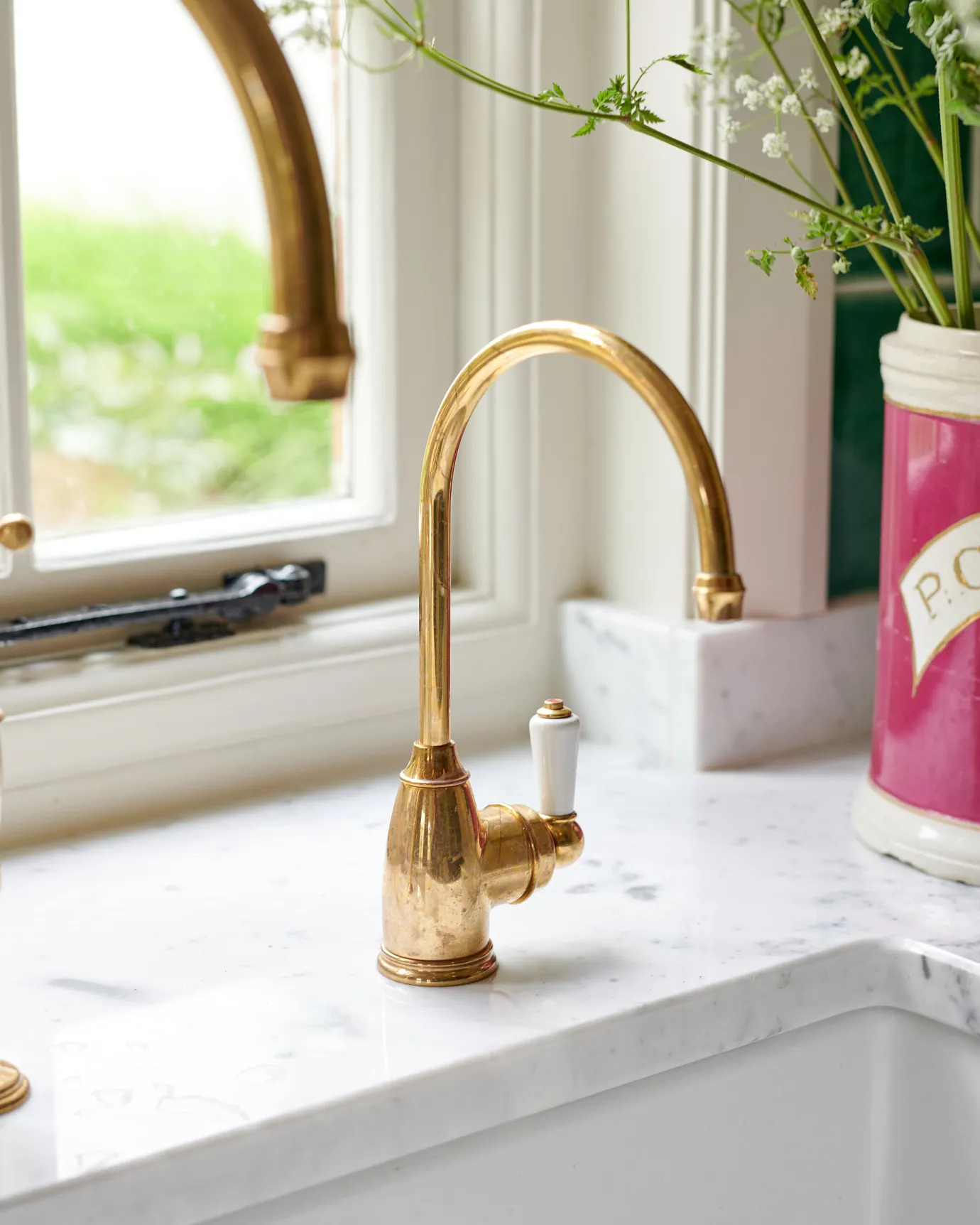 A small traditional-style aged brass tap with a white ceramic lever on a Carrara marble worktop.