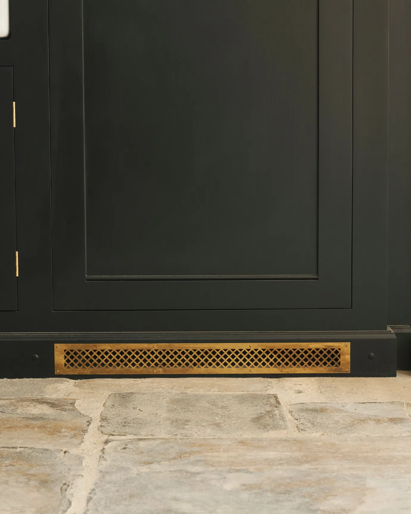 A straight-on view of a black painted Georgian-style kitchen cupboard with a classic brass ventilation cover fitted to the skirting.