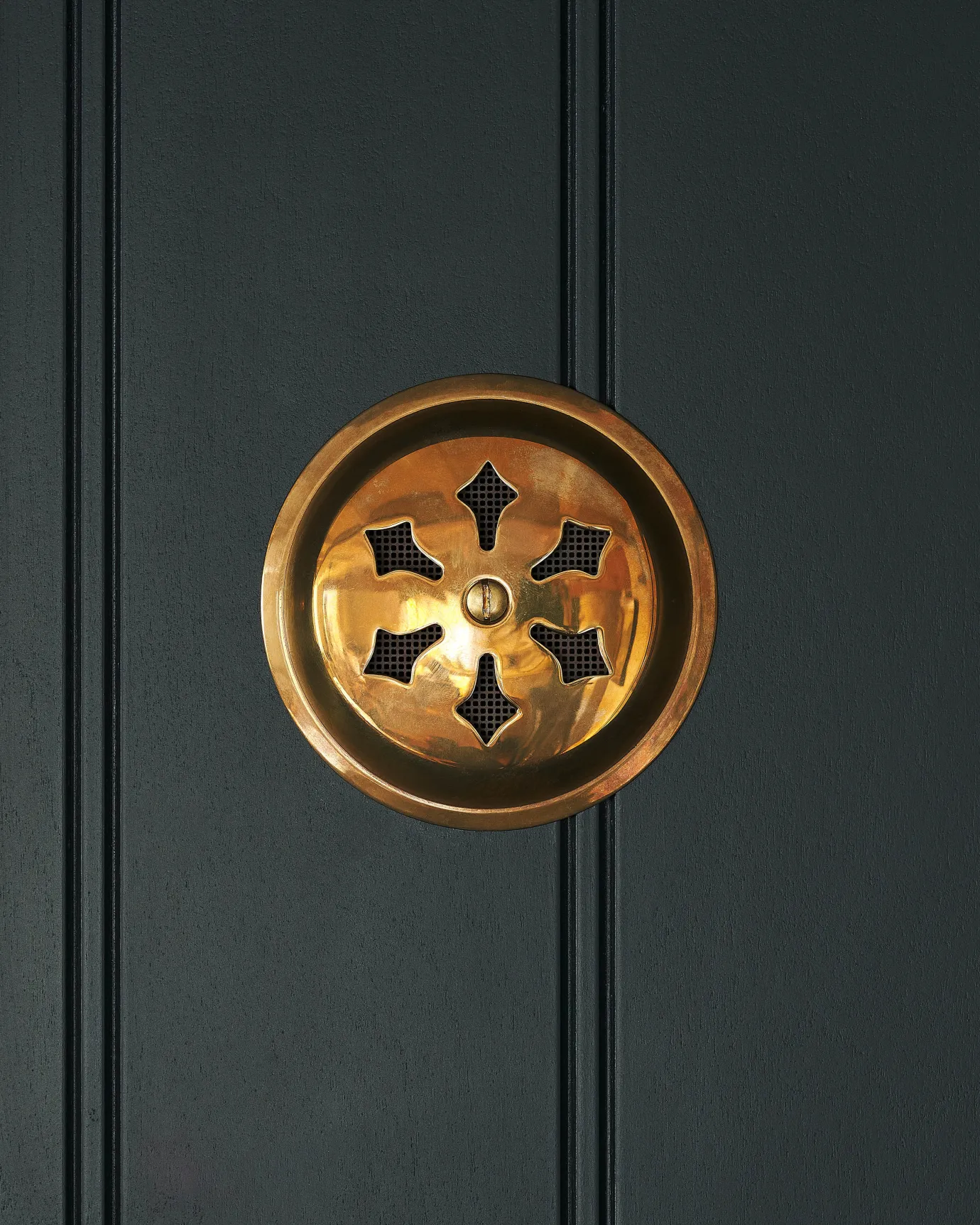 A Victorian-inspired circular brass ventilation grille with traditional decorative cutouts.