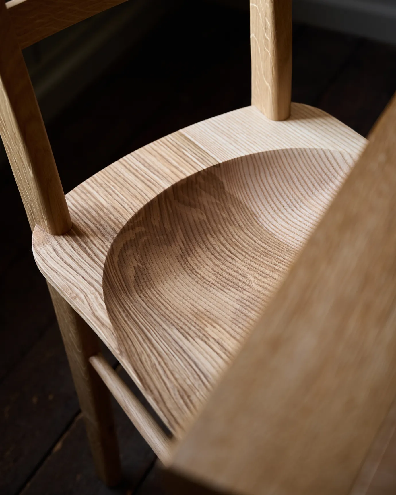 A close-up view of a sculpted ash seat pan from a mid-century-style dining chair.