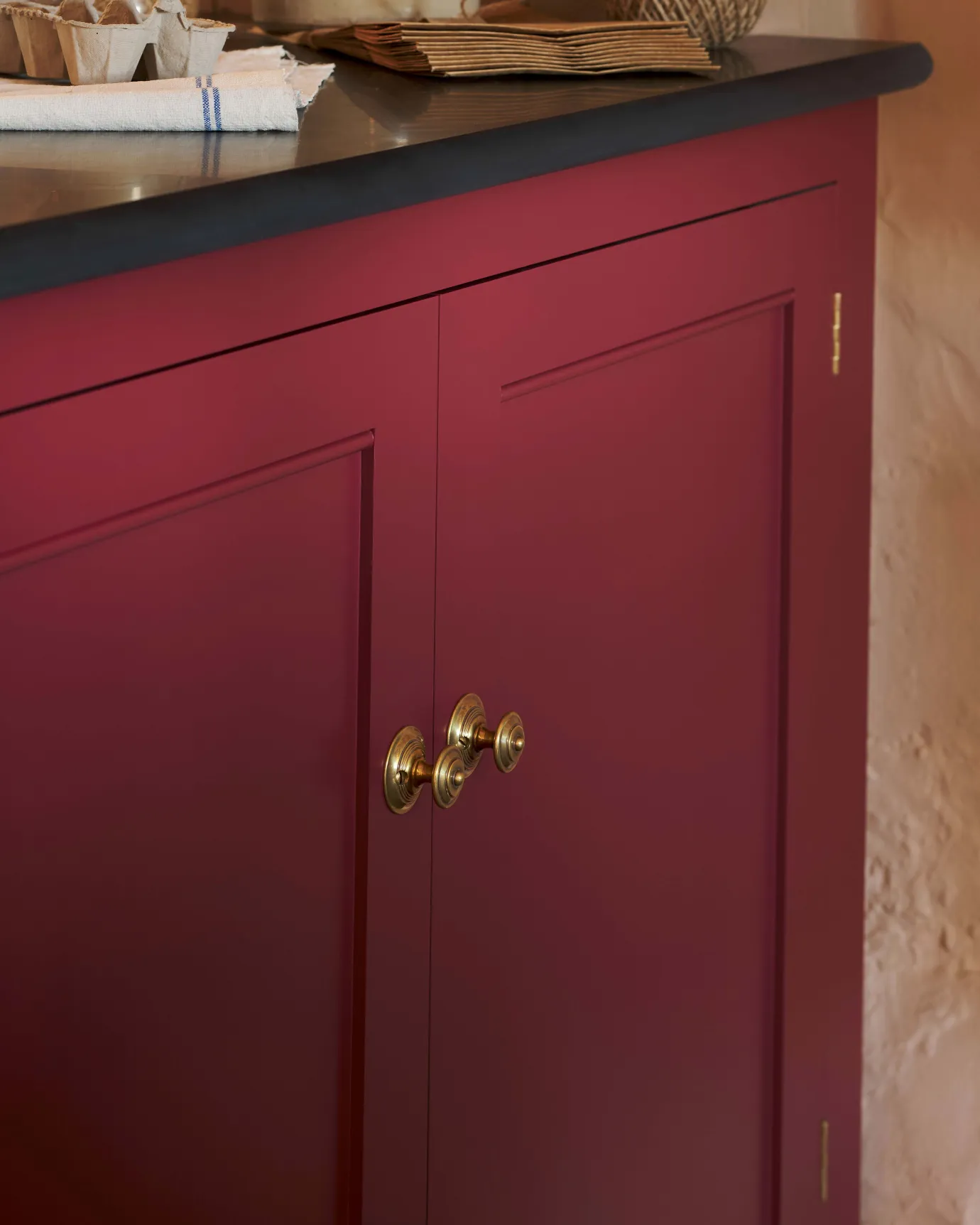 An oblique view of a pair of Victorian-inspired ornate doorknobs in a warm burnished brass finish, fitted to red painted cupboard doors.