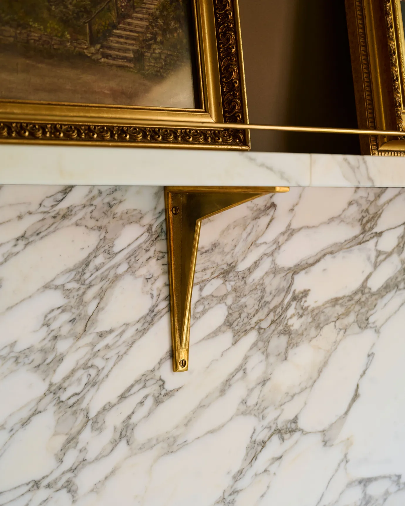 An oblique view of a classic brass utilitarian shelf bracket fitted to an Arabescato marble splashback and shelf.
