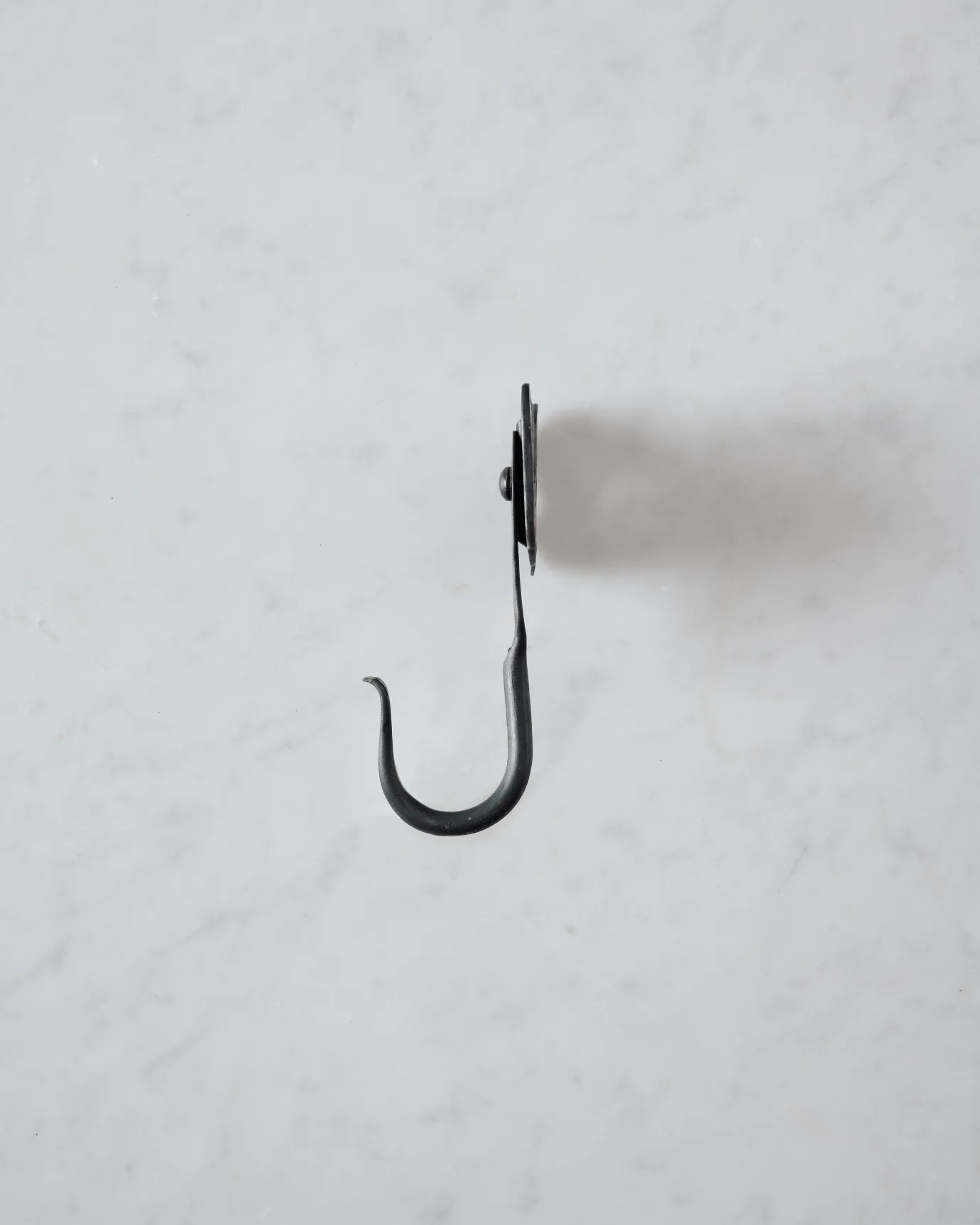 A side profile view of a small iron wall hook with a backplate shaped like elephant ears.