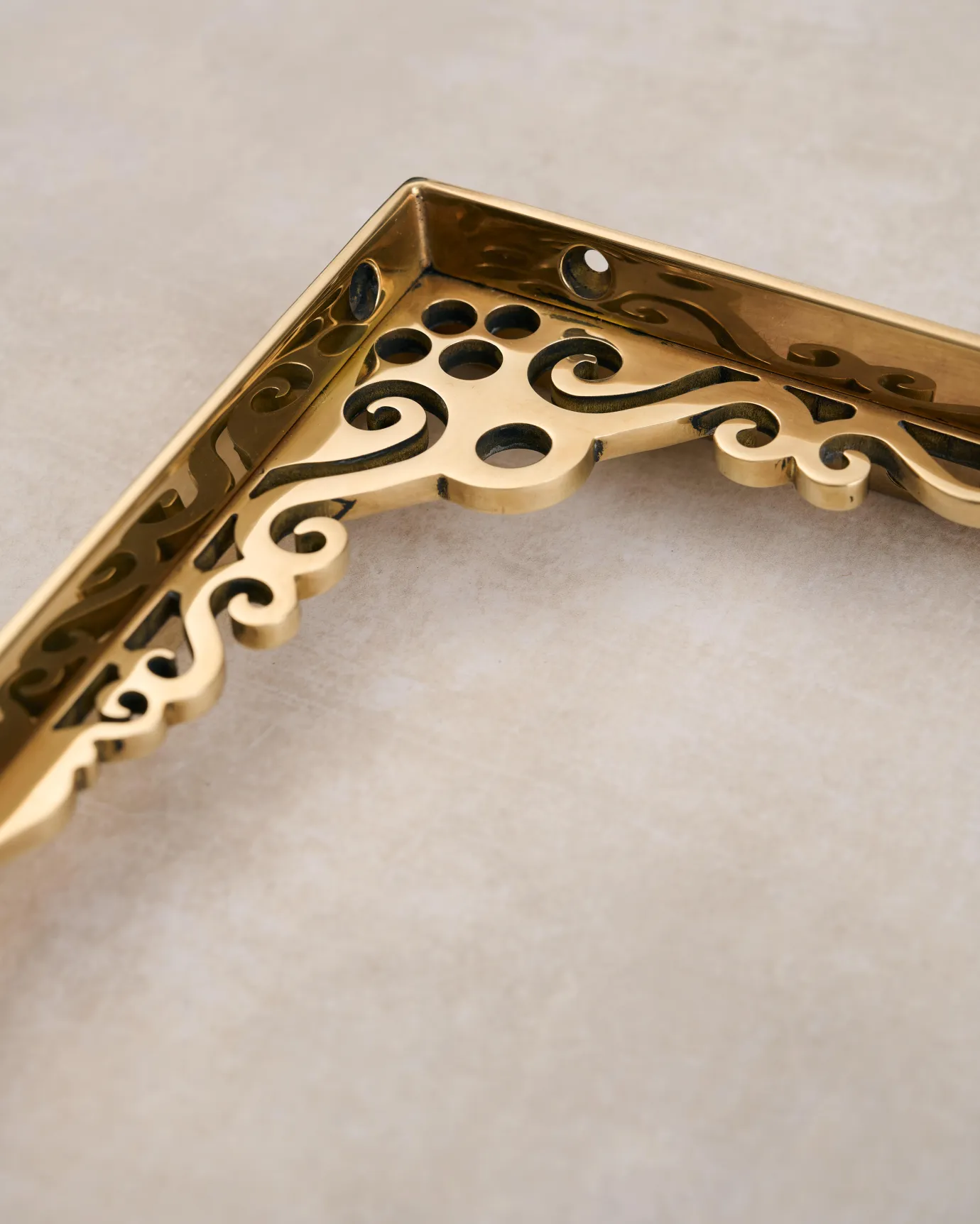 A close-up view of the decorative cutout patterns on a small Victorian-inspired ornate polished brass shelf bracket.