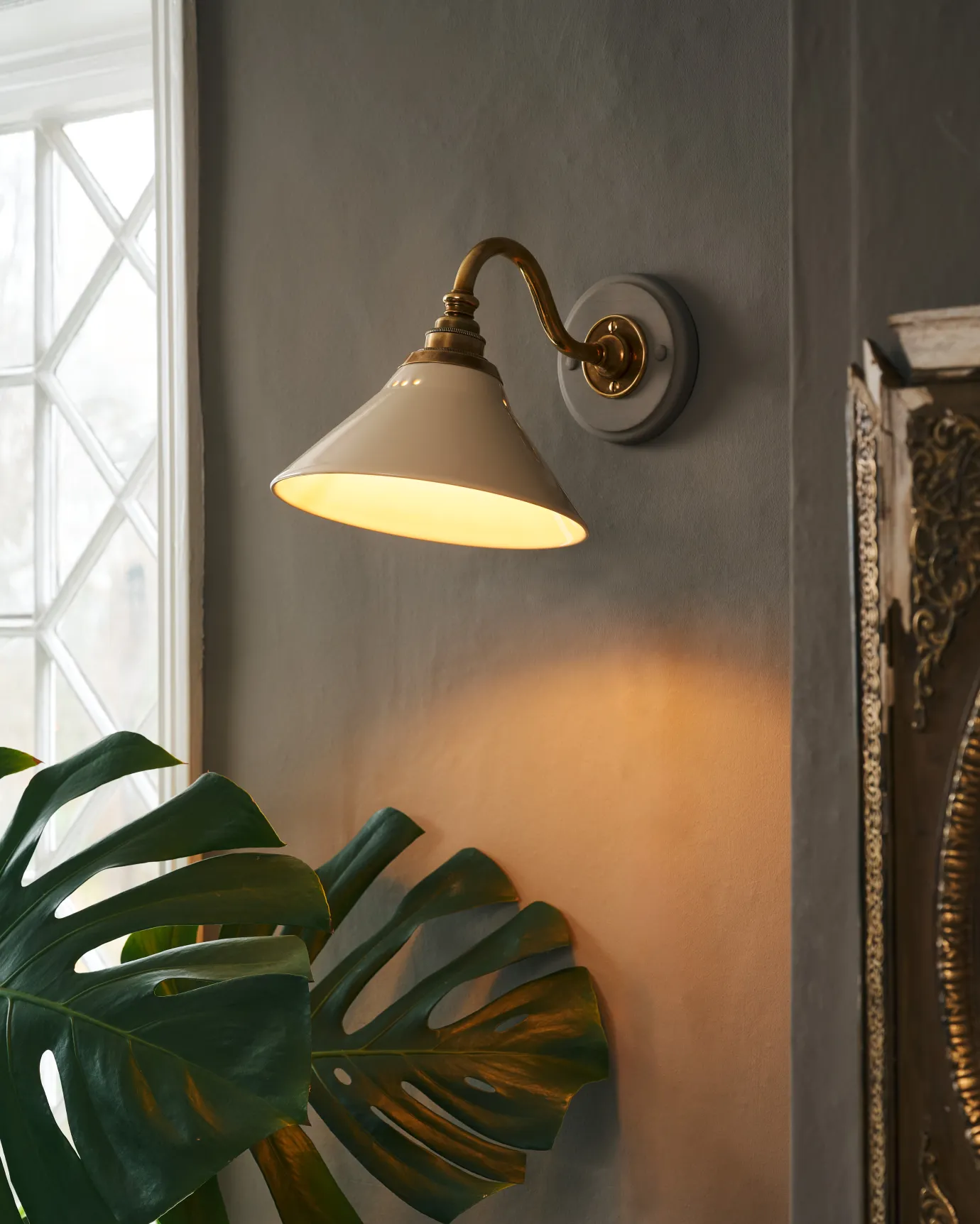 A small Victorian-inspired wall light with a swan neck brass arm and a cream glazed ceramic shade.