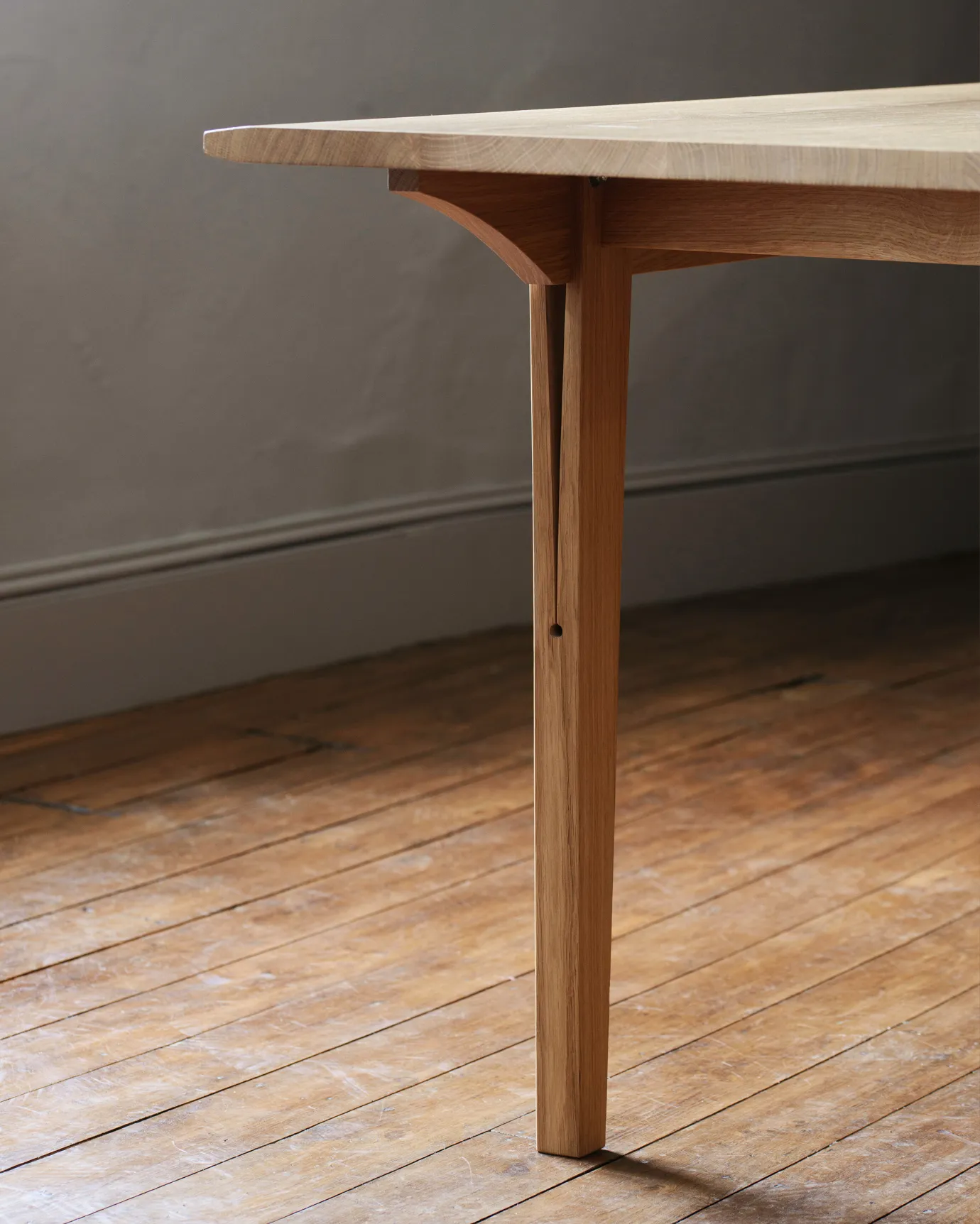 A close-up view of a chamfered oak table leg with a long split design which locks onto the table apron.