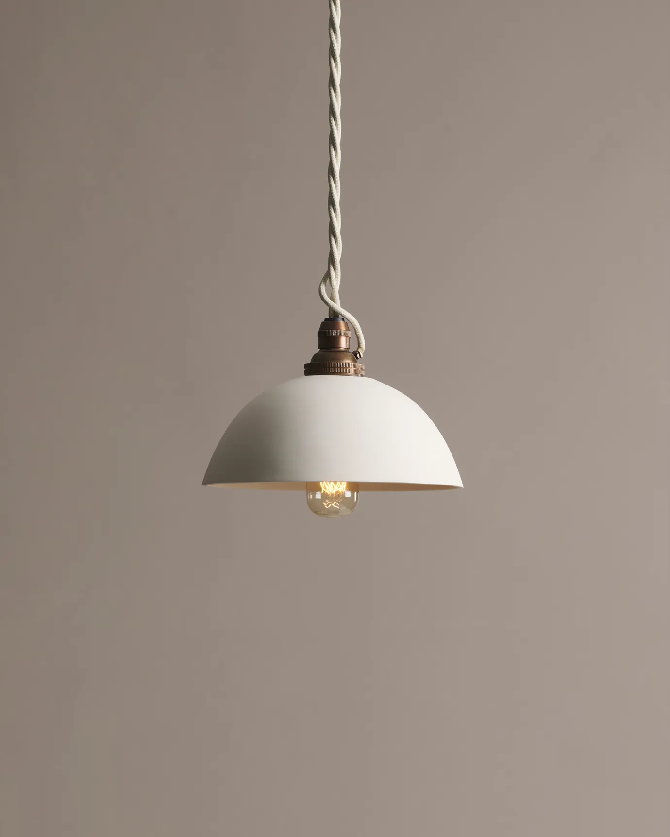 A plain rice bowl porcelain pendant light with an unglazed finish, an aged brass B22 lampholder and a white twisted fabric flex cord.