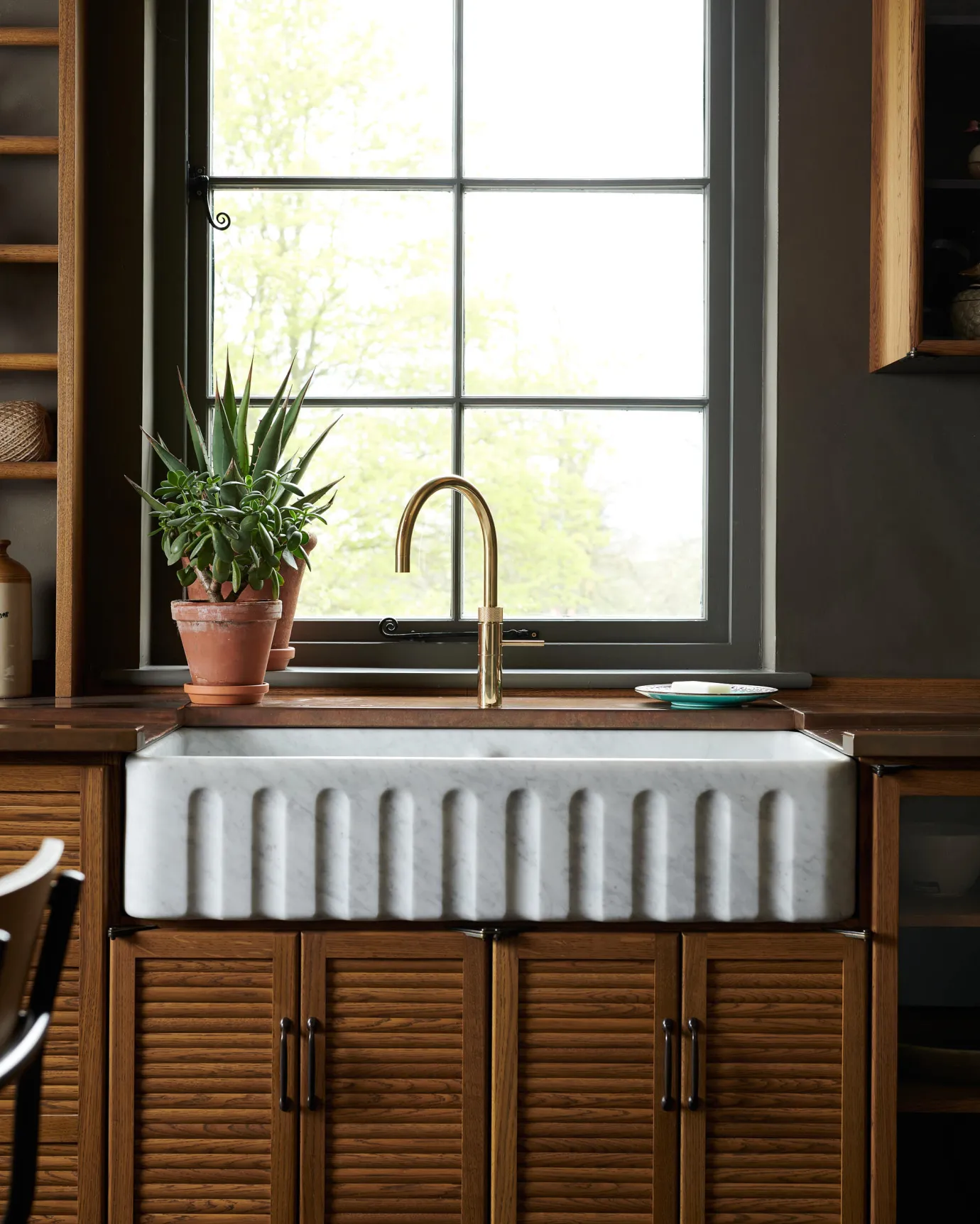 A contemporary-style brass tap in a mid-century-style kitchen with oak cupboard doors, a fluted Carrara marble sink and an aged copper worktop.