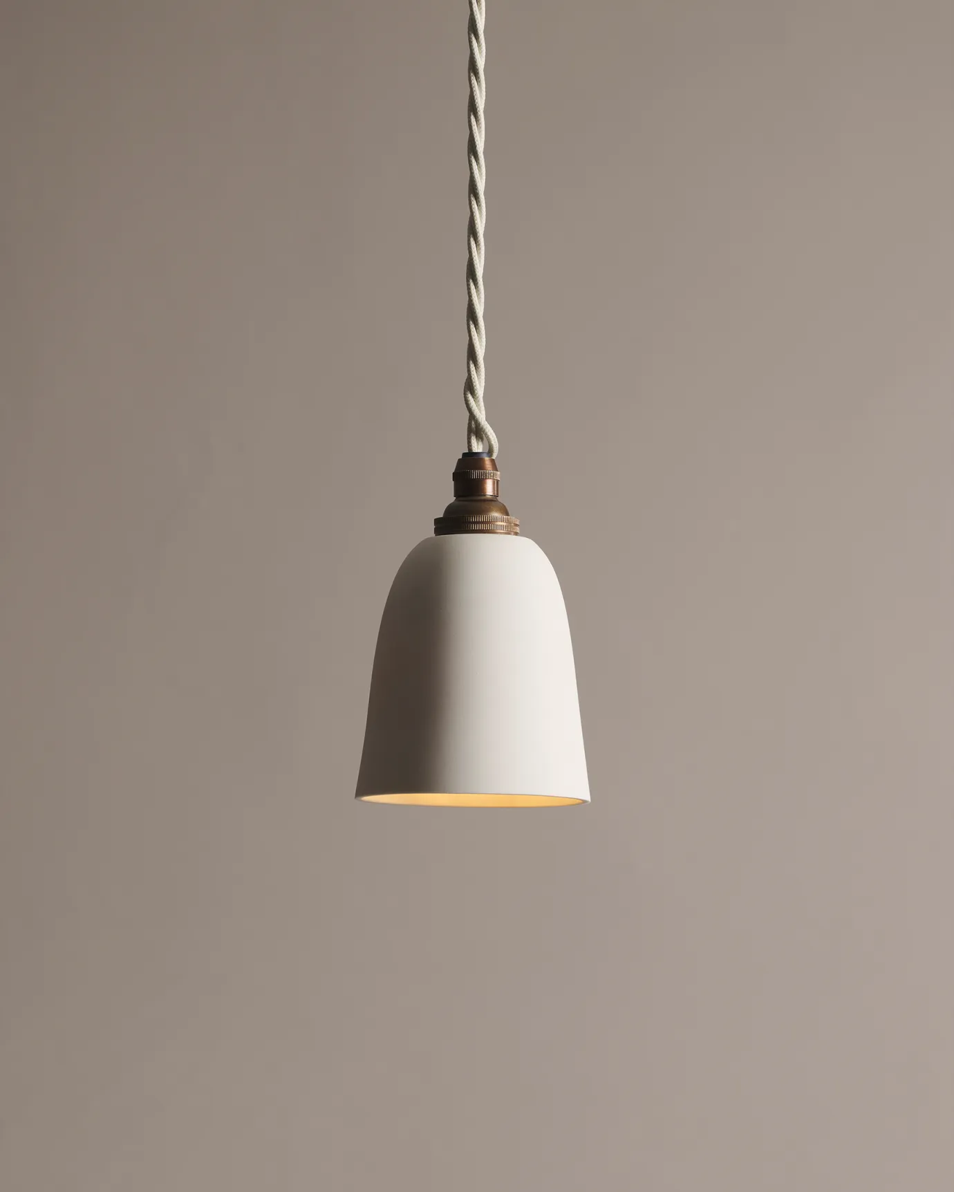 A small plain beaker porcelain pendant light with an unglazed finish, an aged brass B22 lampholder and a white twisted fabric flex cord.