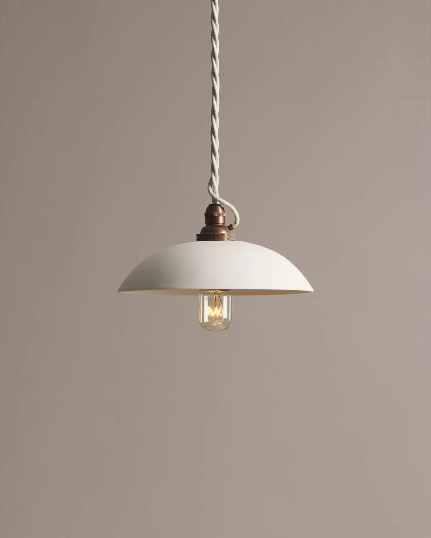 A small plain skullcap porcelain pendant light with an unglazed finish, an aged brass E27 lampholder and a white twisted fabric flex cord.