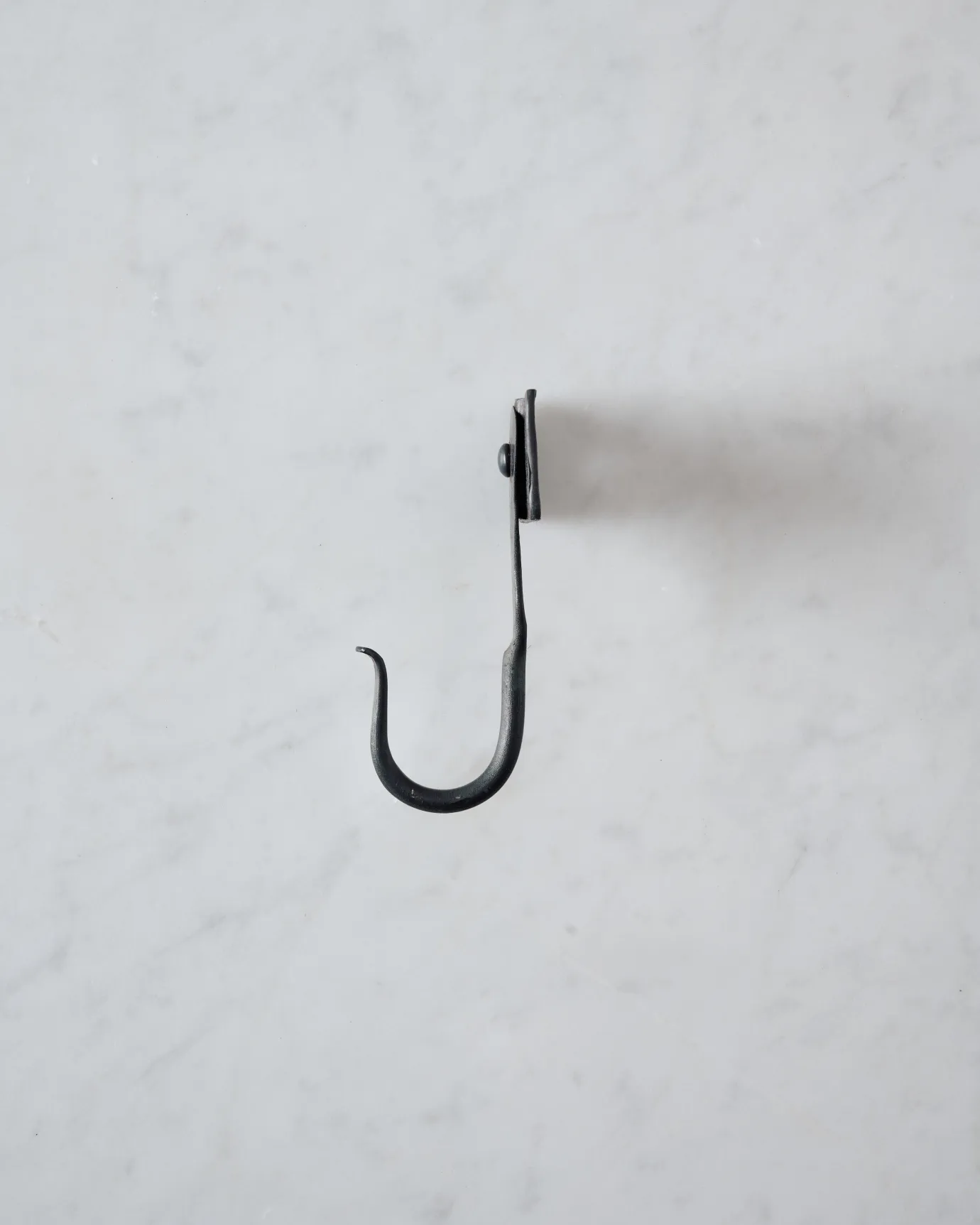 A side profile view of a small iron wall hook with a square-shaped backplate.