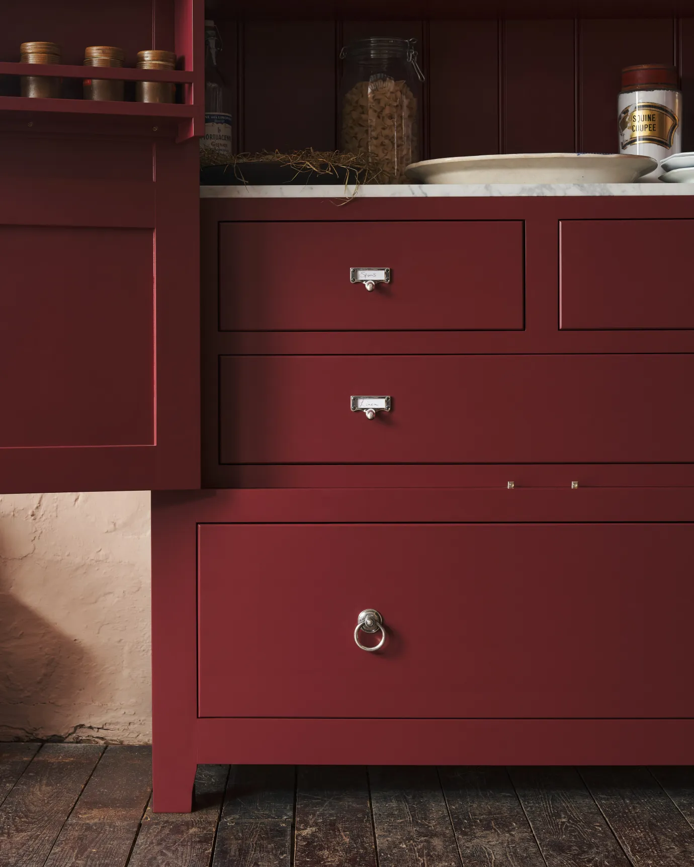 A straight-on view of a red painted Georgian-style pantry cupboard with a bottom drawer fitted with a Victorian-inspired ring pull handle in a tarnished silver finish.